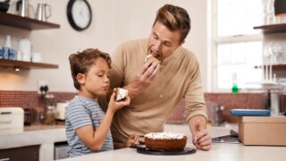 Eating, cake and father with child in kitchen at home with sweet treat for breakfast or snack. Happy, bonding and dad enjoying dessert with boy kid for morning meal or craving together at house.