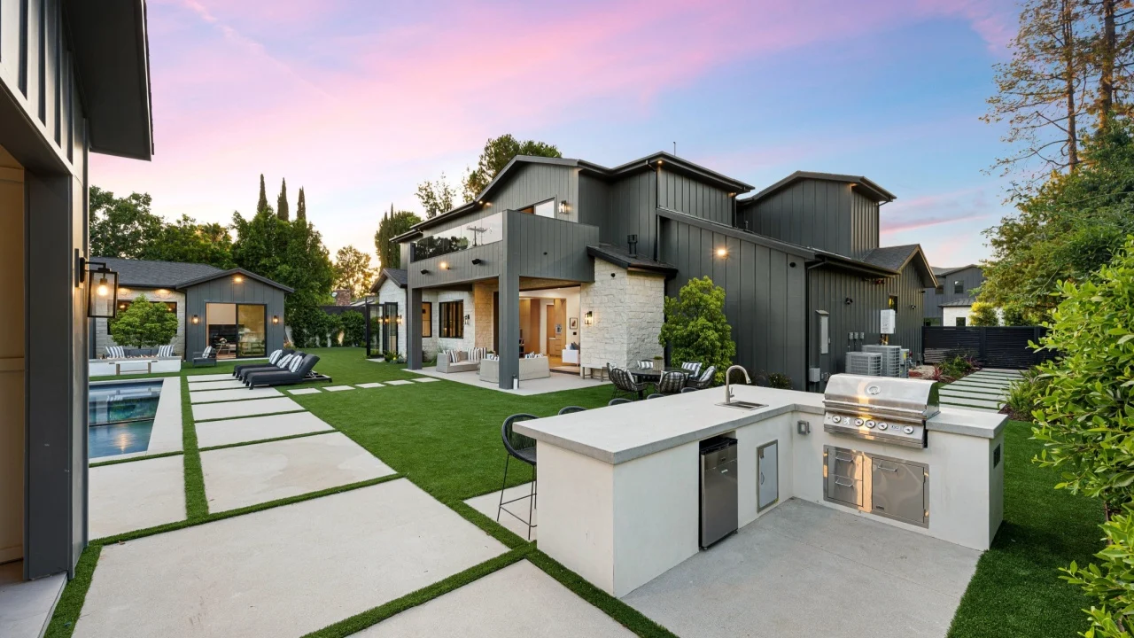 Modern backyard with outdoor kitchen, swimming pool, and lounge area at sunset.