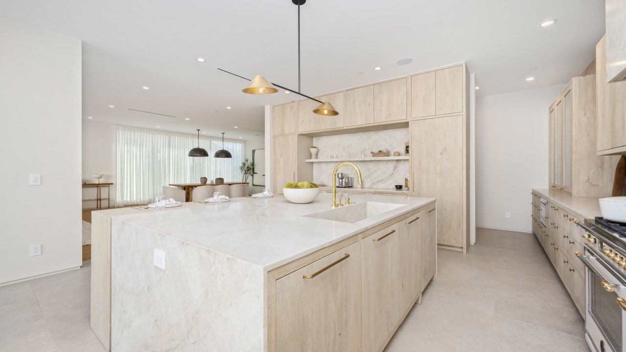 Modern minimalist kitchen with light wooden cabinetry, marble countertops, and gold accents in a bright, open space.