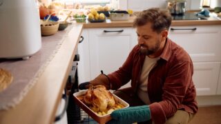 Happy man turkey in the oven while roasting it for Thanksgiving dinner in the kitchen.