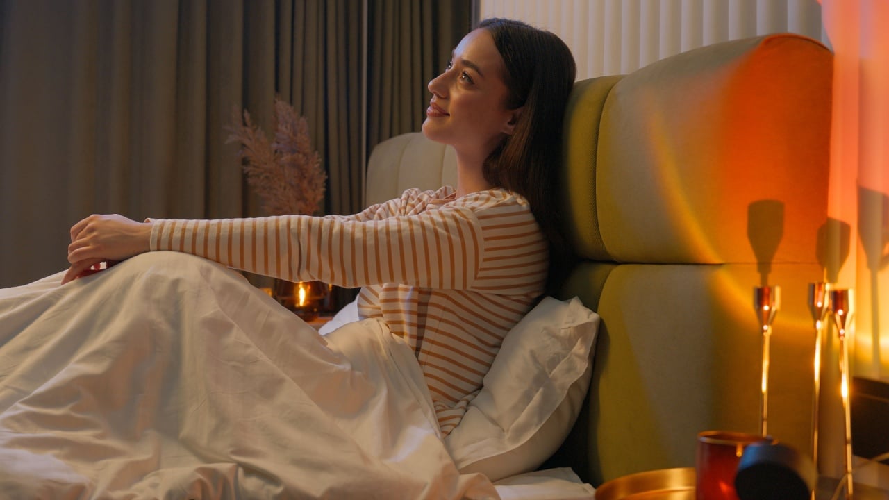 Happy Caucasian woman sitting on bed bedroom home comfortable smiling pleasure rest weekend joy girl female cozy relaxing bedtime sleep night hotel positive apartment satisfaction homeowner wellbeing