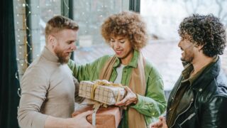 A multi ethnic group of friends giving each other a craft paper wrapped gifts indoor near the door. Holiday time concept.