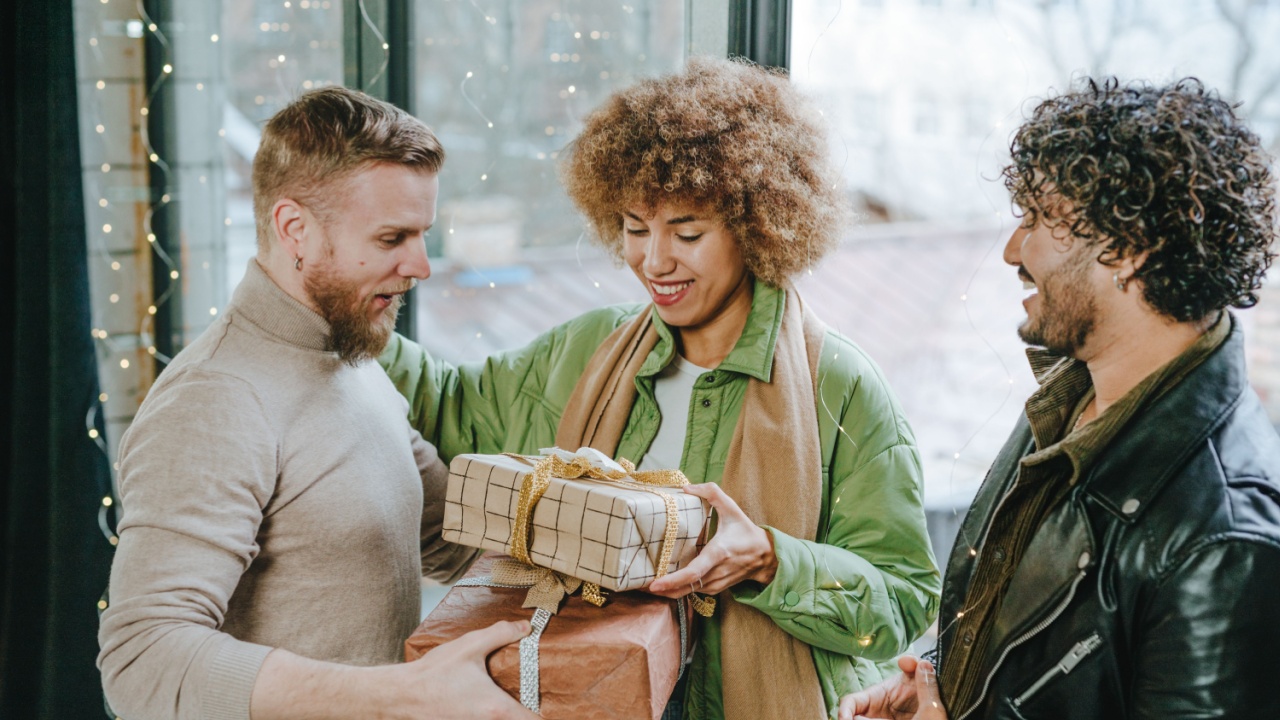 A multi ethnic group of friends giving each other a craft paper wrapped gifts indoor near the door. Holiday time concept.
