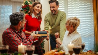 Young woman is giving a christmas gift to her father during a festive family dinner. They are all smiling and happy to be together for the holidays