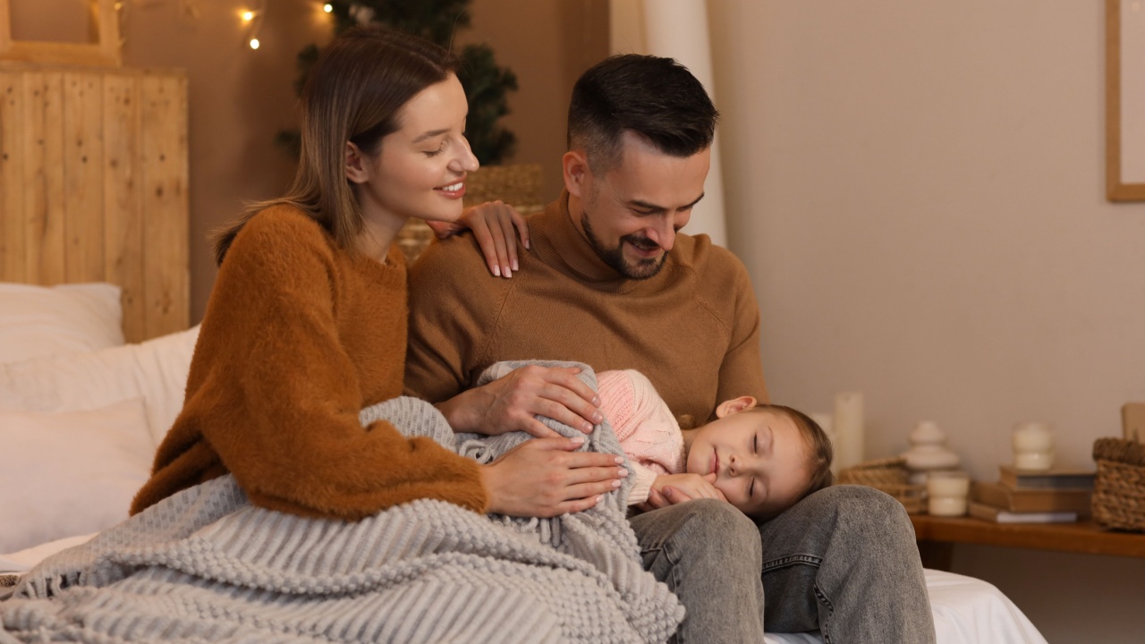 Happy parents and their little daughter sleeping on bed in winter evening at home