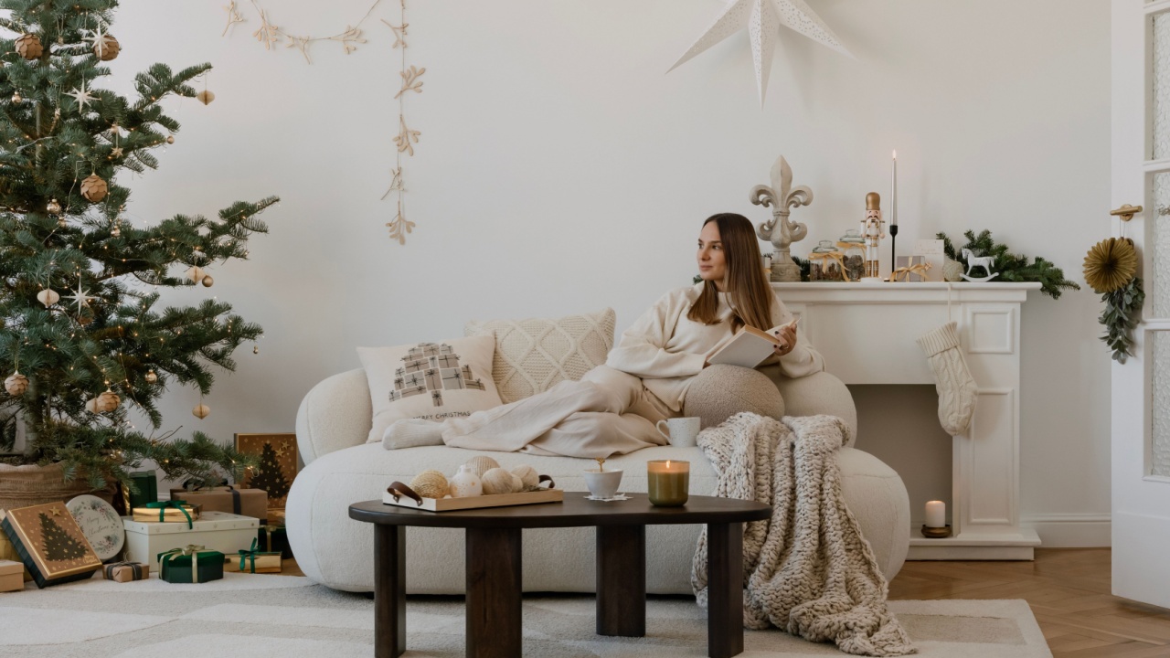 Bright and neutral compositions of a living room with Christmas tree and decorations. A young woman sits on the sofa by the Christmas tree and reads a book. Winter is coming. Home decor. Template. 