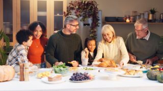 Happy family, serving chicken and thanksgiving with children, event and food for holiday or vacation. Feast, people and interracial parents at dinner party, reunion and gathering for bonding in home
