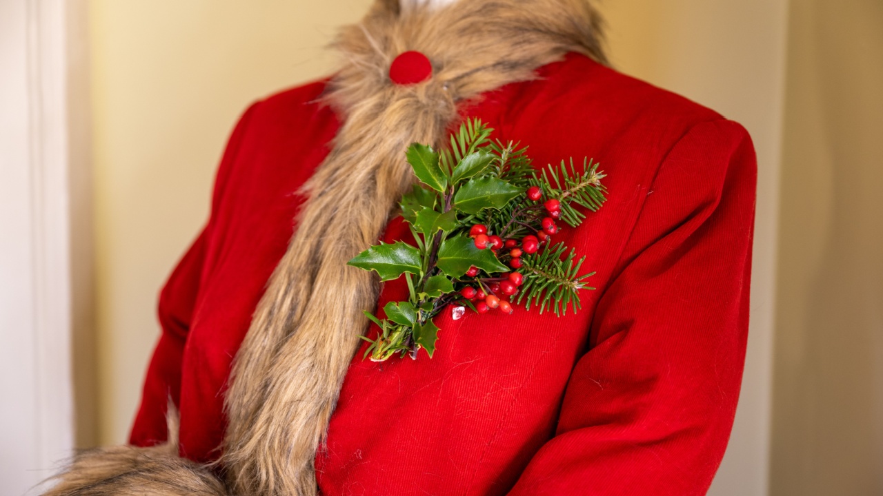 A vintage bright red felt woman's coat with a faux fur collar and strip down the center of the jacket. There's a homemade natural ivy, red berry and evergreen corsage pinned to the breast of the coat.