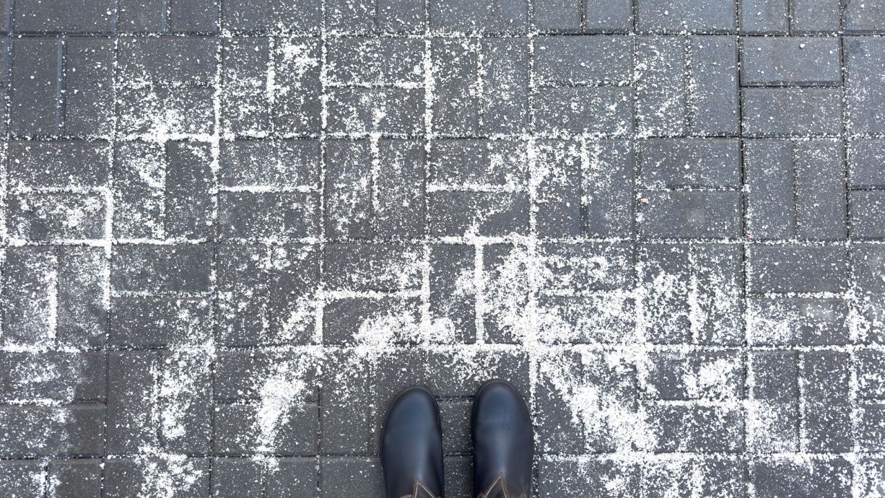 Anti-icing chemicals in winter season. Top view of winter boots and road strewn with technical salt or reagents to prevent icing. Effective tool to fight ice on surfaces. Rock salt on road. 