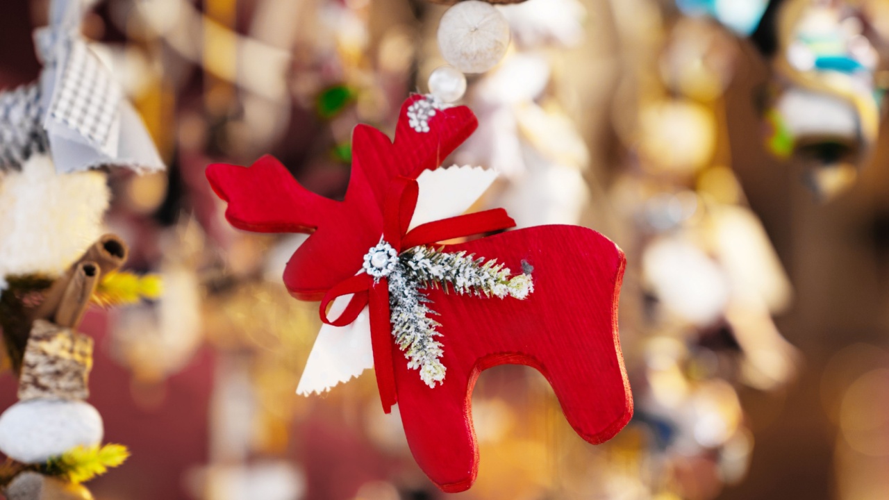 Red wooden reindeer ornament decorated with ribbon and pine branch, hanging amidst colorful festive decorations in soft lighting highlighting holiday charm