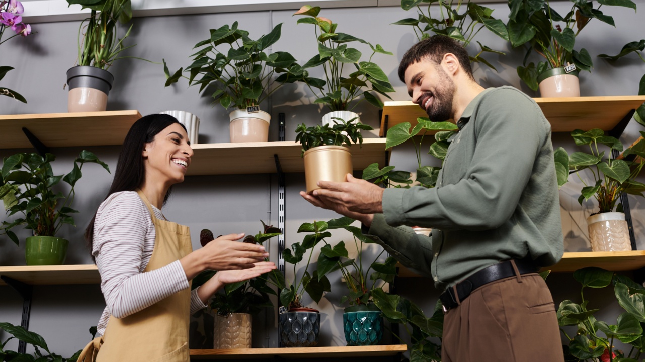 A skilled florist shares her passion with a client while surrounded by lush greenery.