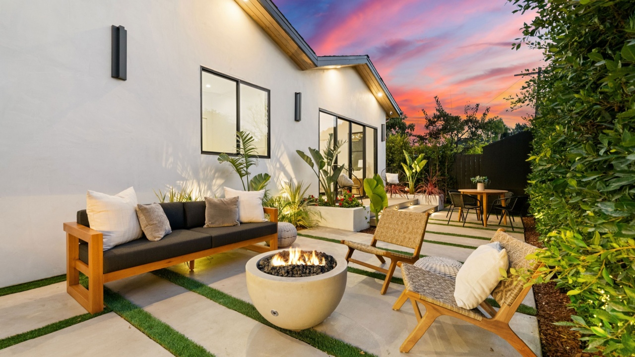 Modern outdoor patio with cozy seating and fire pit, set against a vibrant sunset sky, showcasing contemporary design and lush greenery.