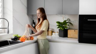 A young woman takes out organic vegetables and fruits from a reusable bag in the modern kitchen. Grocery shopping. Zero Waste. Eco-Friendly Shopping. The concept of a healthy lifestyle