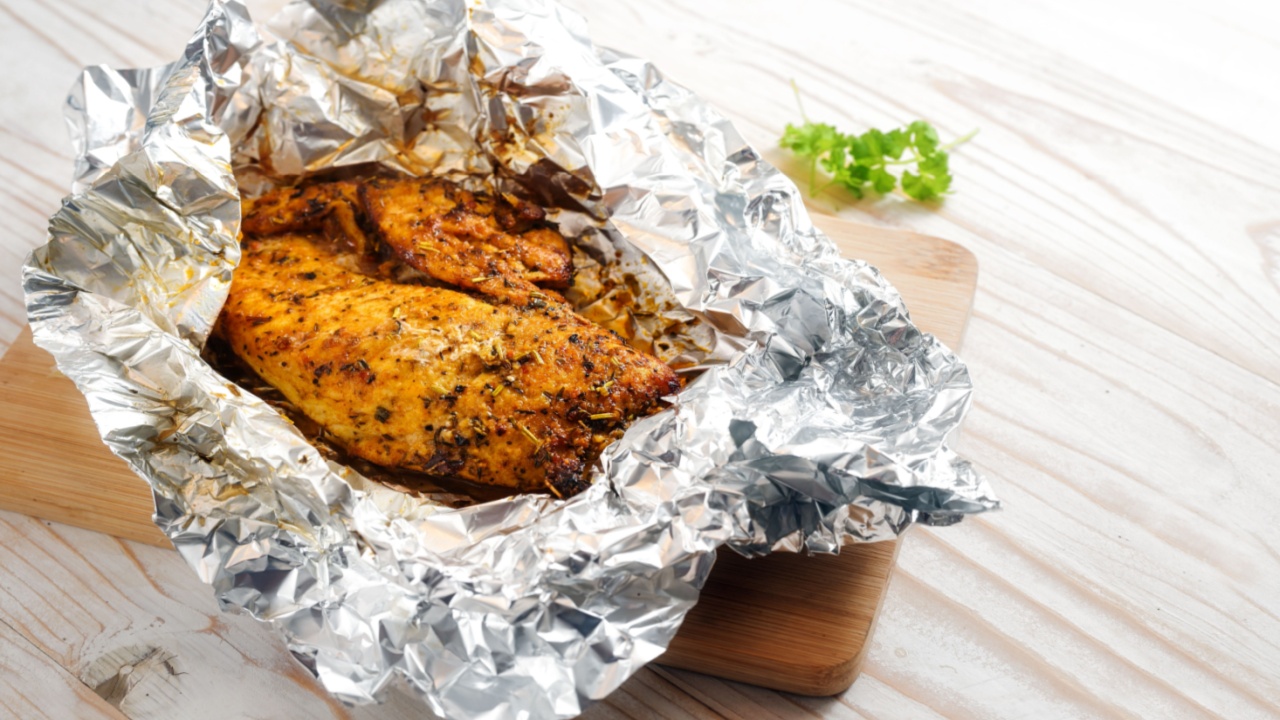Chicken breast fillet, juicy roasted with spices and herbs in aluminum foil on a cutting board and a light wooden table, cooking a tasty meat dish, copy space, selected focus, narrow depth of field