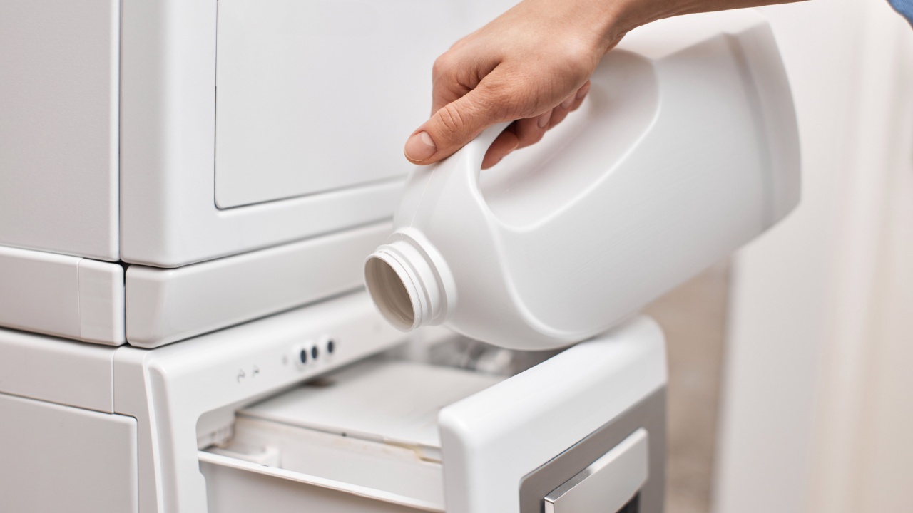 female hand pouring liquid laundry detergent from bottle into washing machine, closeup