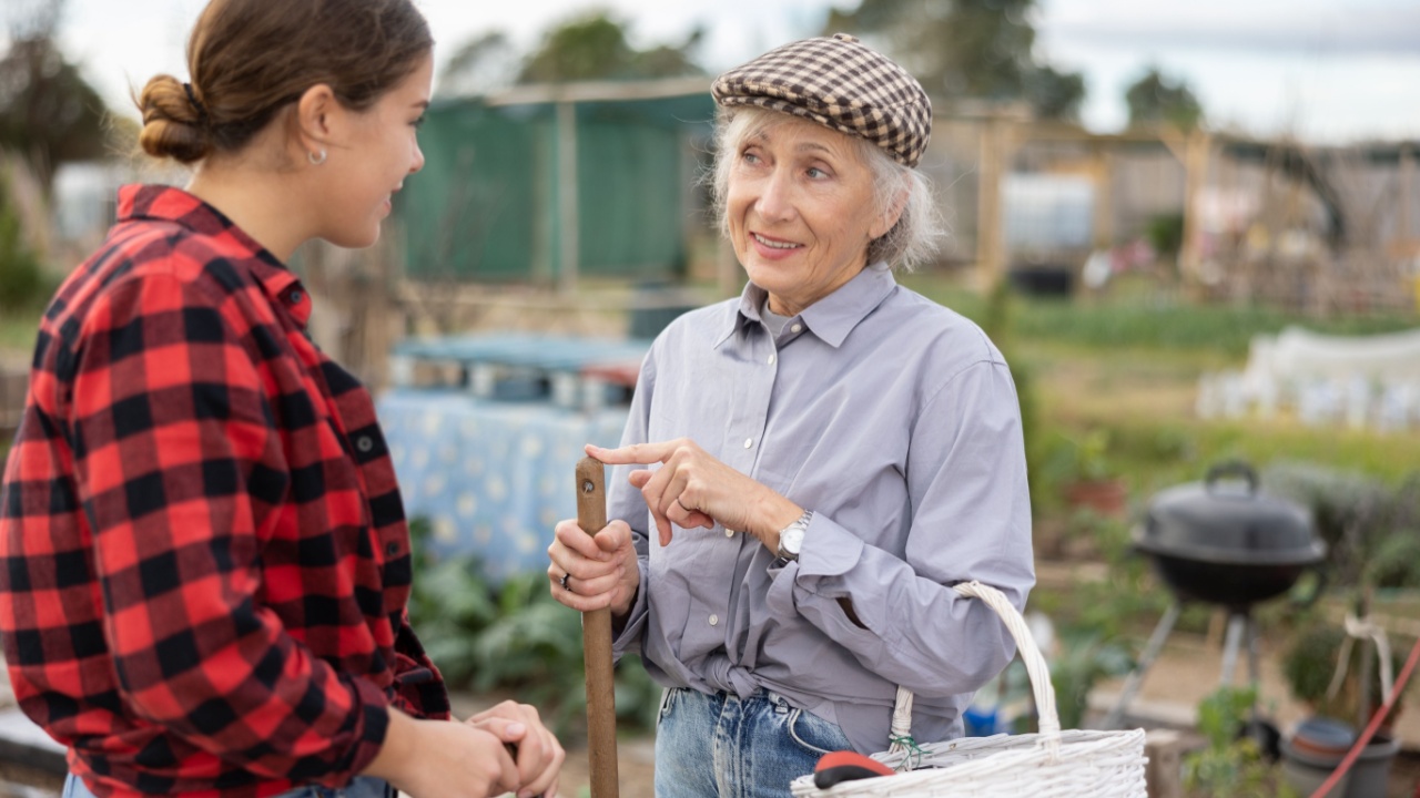 Two female farmers friendly talking outside next to wooden fence on background with farm