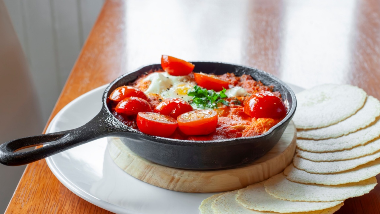 Shakshuka with cherry tomatoes, eggs, and arepas served in cast iron skillet