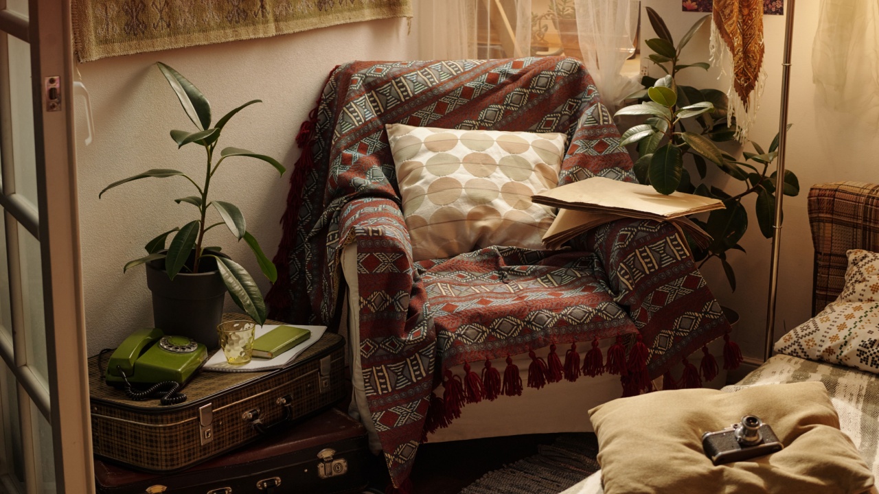 Cozy reading nook with an armchair draped in patterned throw and stacked cushions. Vintage items like an old phone and suitcase enhance nostalgic ambiance of room