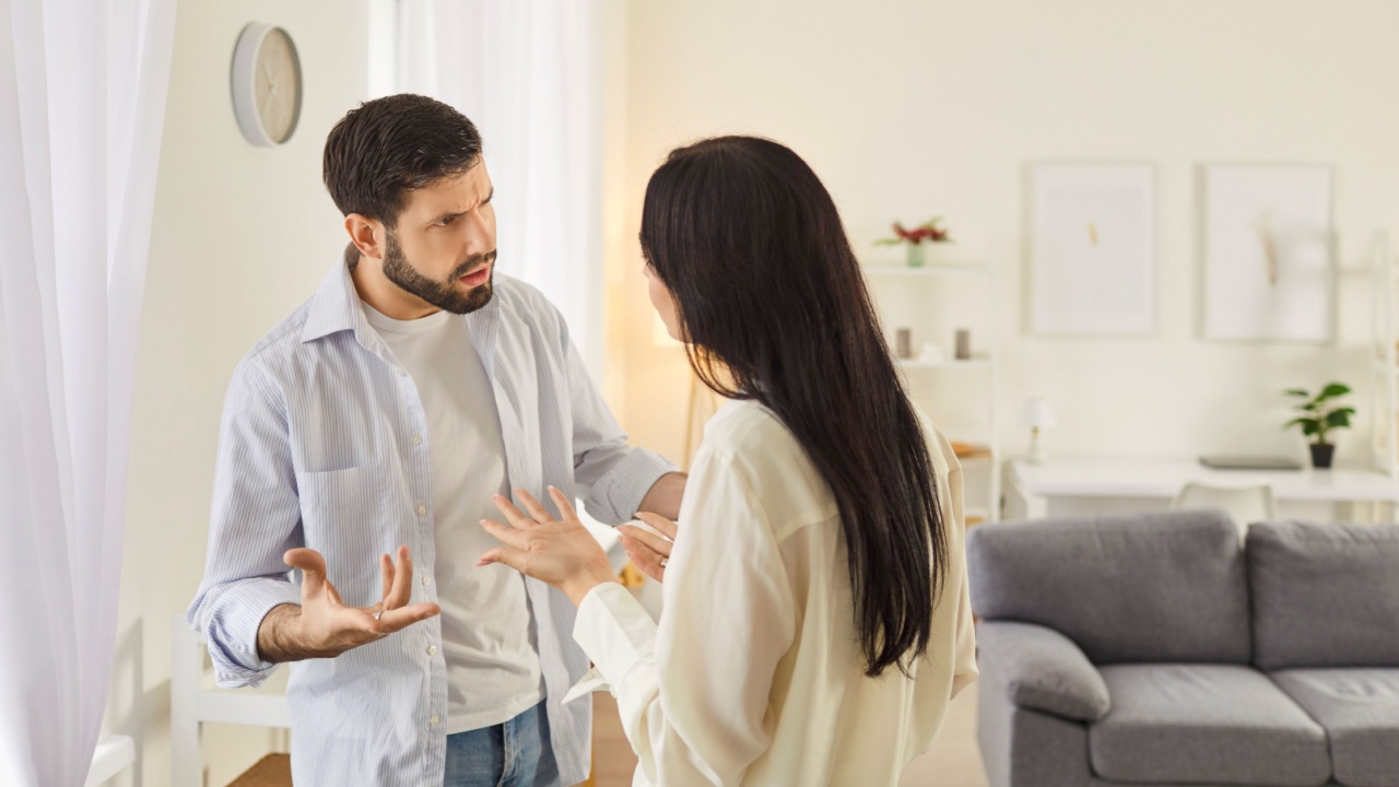 Young family couple arguing in living room, showing signs of disagreement. Angry husband and wife quarreling, expressing frustration and disappointment. Relationship problems