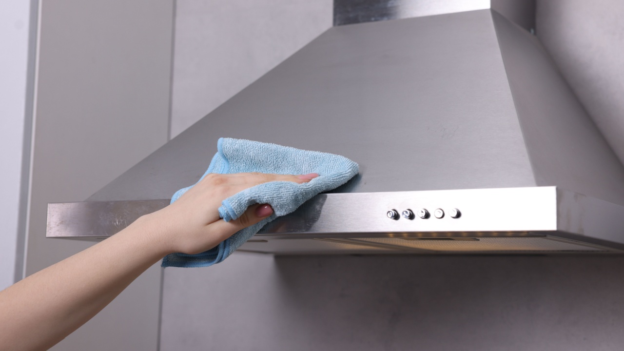 Woman cleaning kitchen hood with rag indoors, closeup