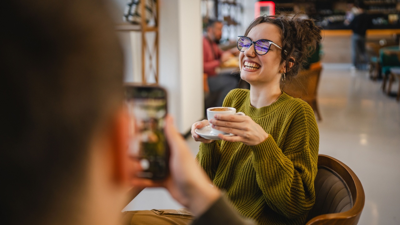 boyfriend use mobile phone to take a photo, or to record v-log of his girlfriend while she drink coffee at cafe