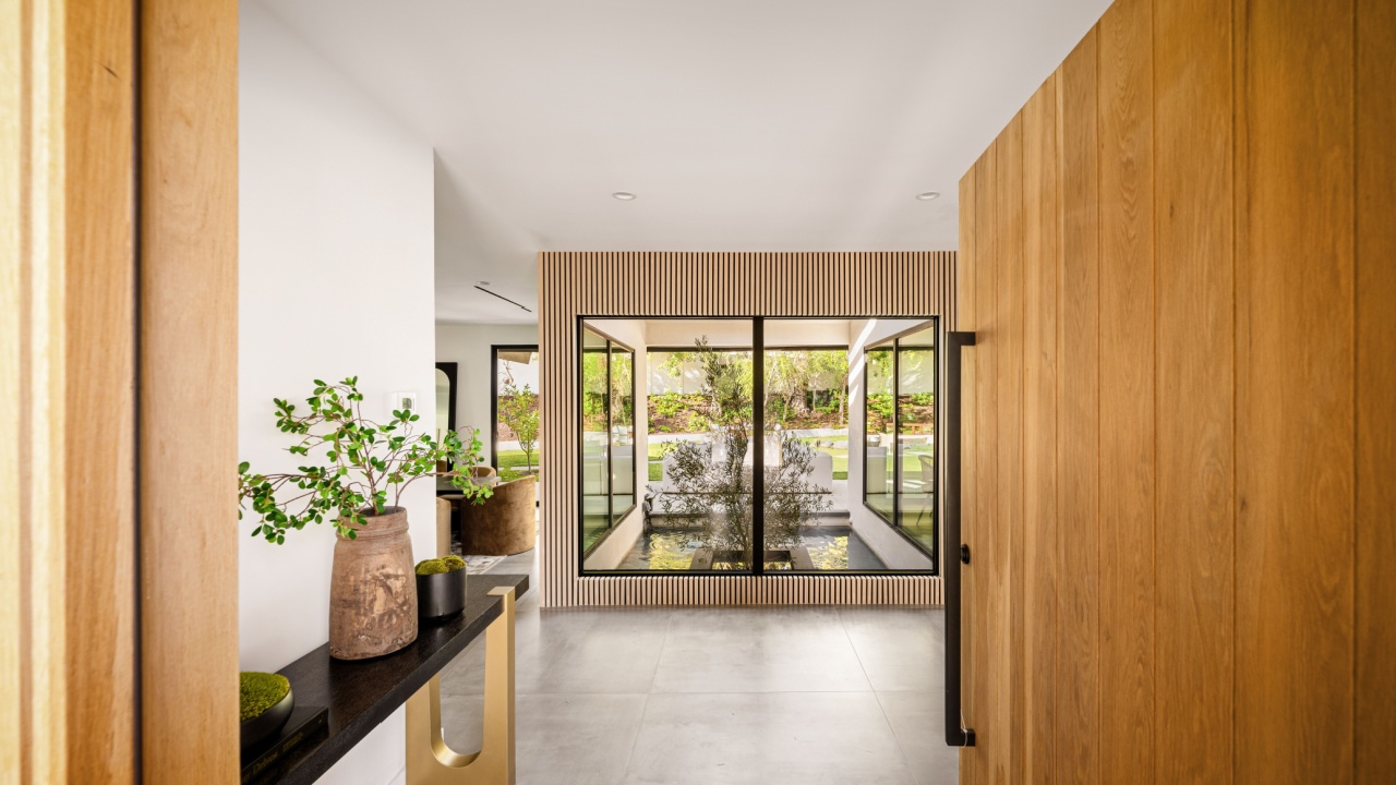 Stylish modern entryway with wood paneling, large glass windows, and a serene water feature for a sophisticated ambiance.