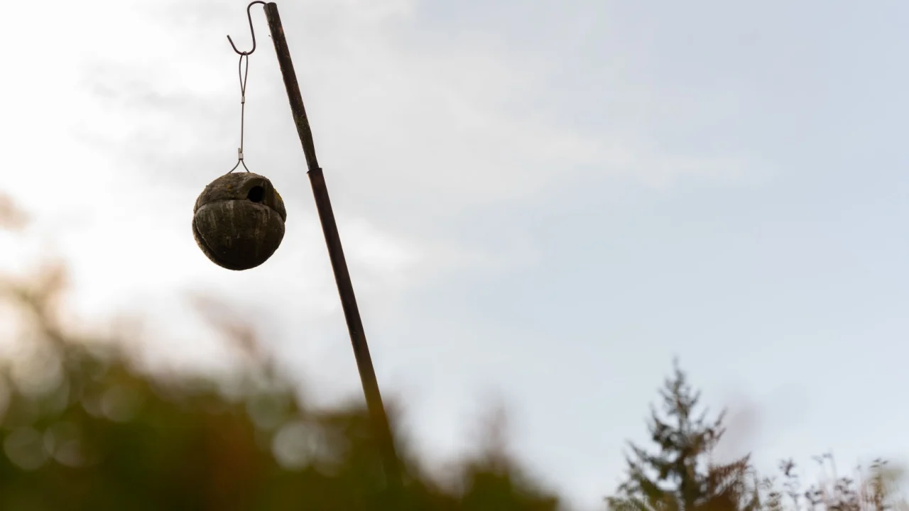 A selective focus shot of a sphere birdhouse hanging on a pipe