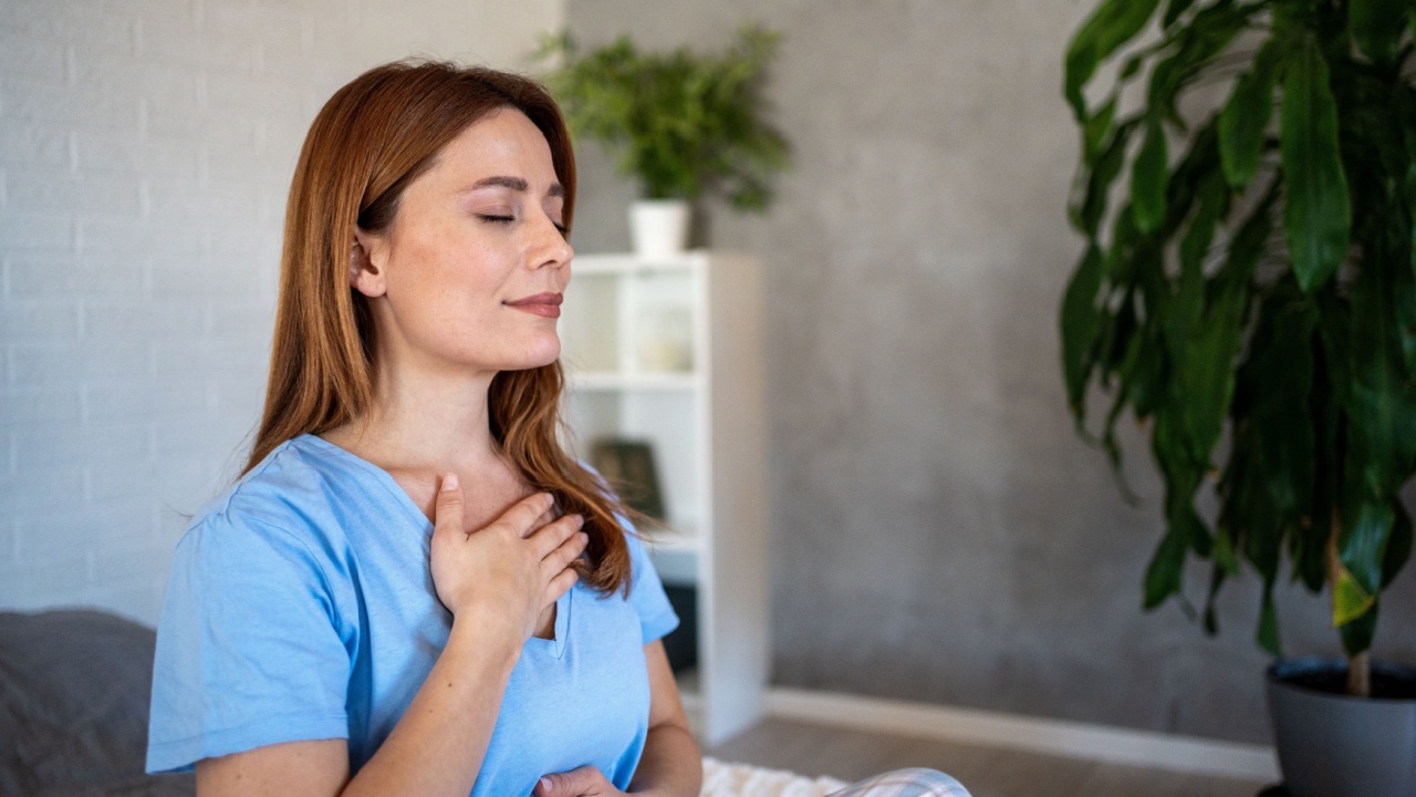 Sitting on her bed with closed eyes and a peaceful expression, a woman practices mindful breathing, promoting relaxation and inner peace in her cozy bedroom