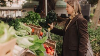 Middle-aged woman on the local Farmers market. Mature Female Customer Shopping At Farmers Market Stall. Beautiful woman buys a greens and vegetables. Close up. Part of the series