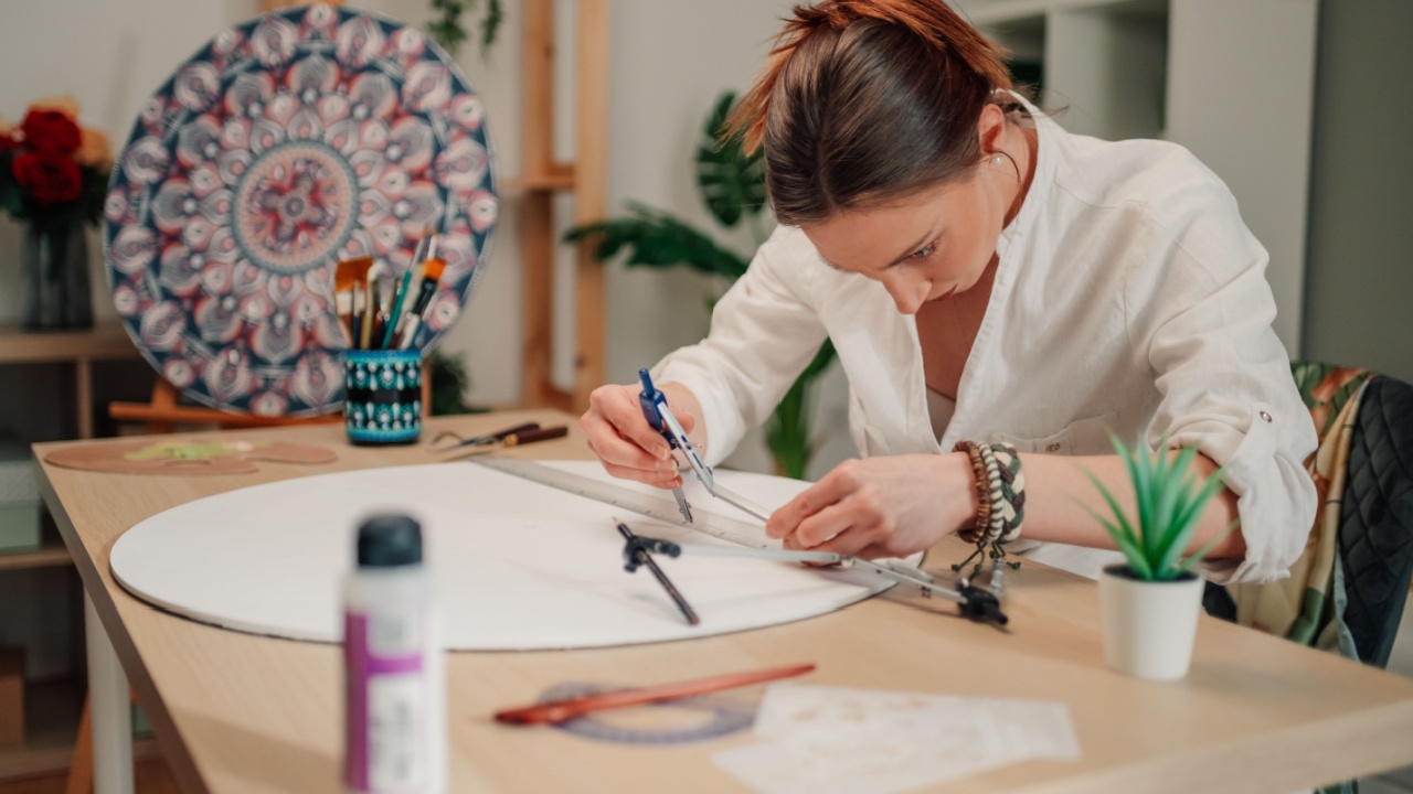 Female artist focusing intently on drawing a mandala with a compass and ruler on a circular canvas, skillfully preparing for vibrant painting in her lively art studio
