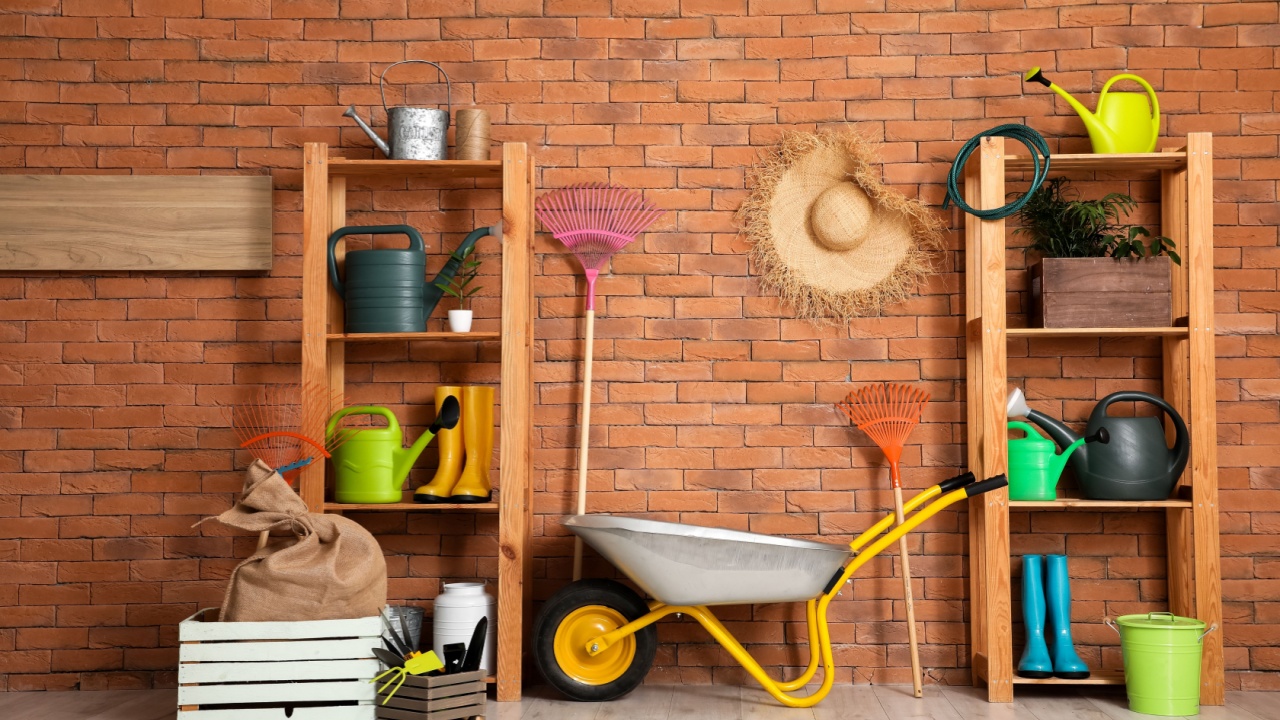 Wheelbarrow, shelving units and gardening tools near brick wall in barn