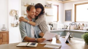 Home, hug and couple with documents, smile and payment for mortgage, rent and love. Apartment, finance and man with woman in kitchen, embrace and paperwork report for savings and investment growth
