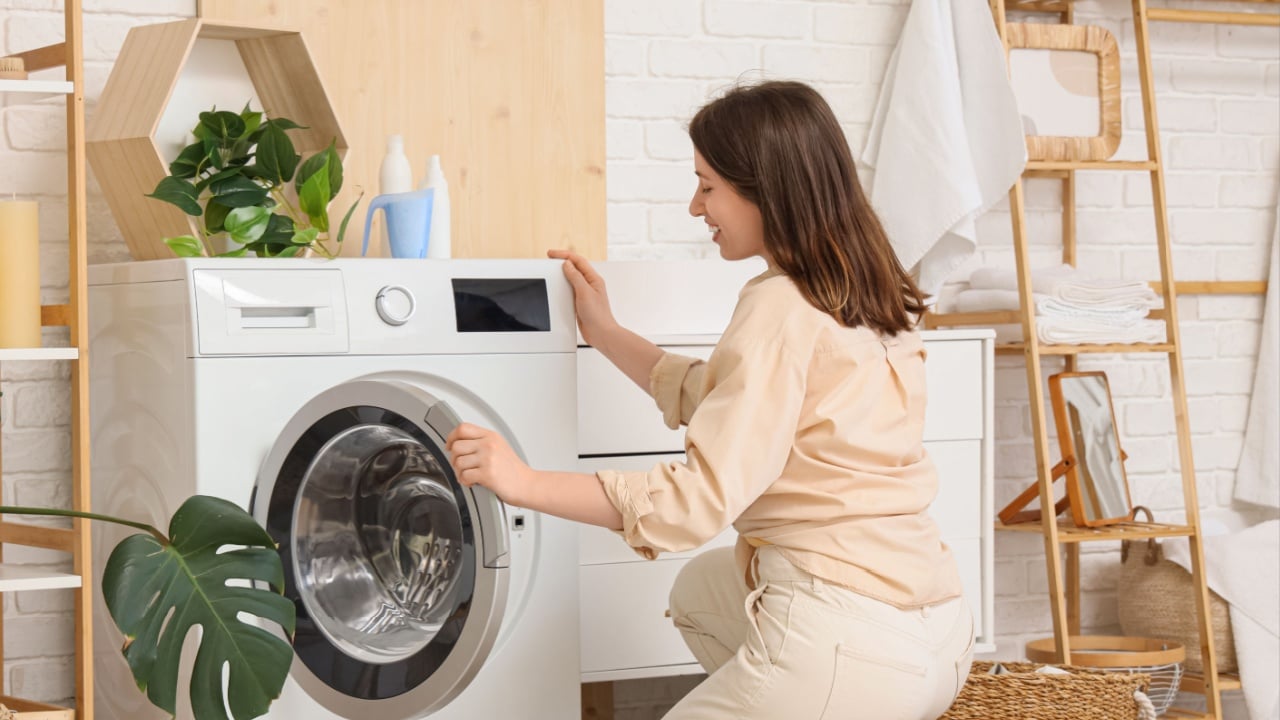 Young woman opening modern washing machine in laundry room