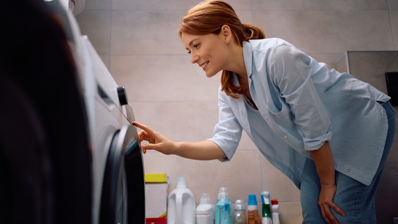Happy woman adjusting timer on washing machine while doing laundry,