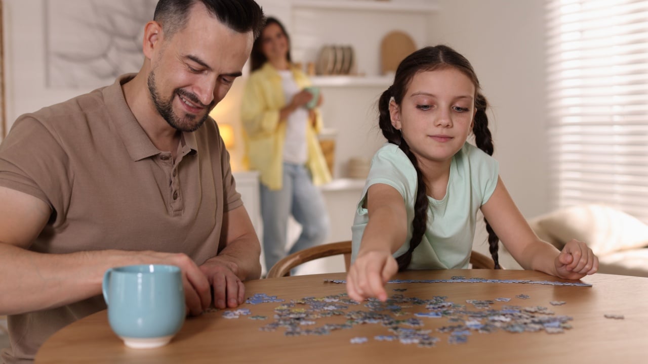 Happy father and his daughter solving puzzle together at wooden table indoors, selective focus