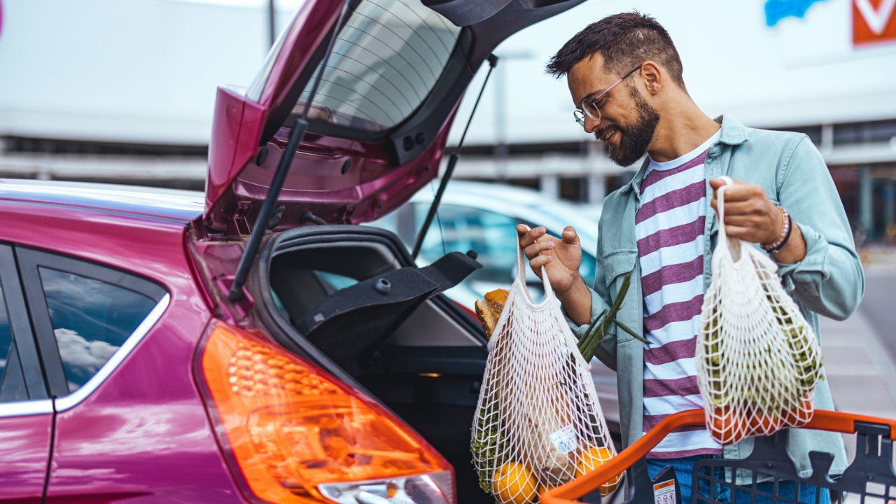A man unloading groceries into a car trunk using reusable eco-friendly mesh bags, representing sustainable shopping.