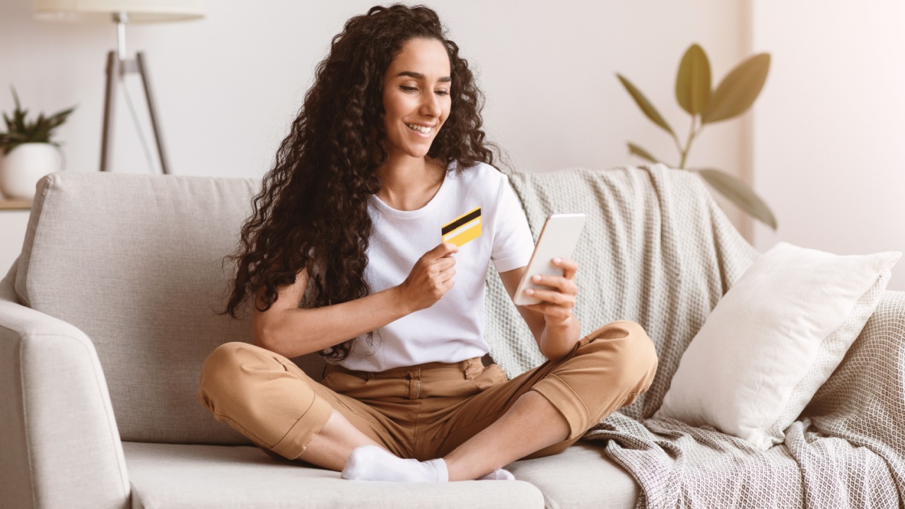 Happy woman using mobile phone and credit card at home