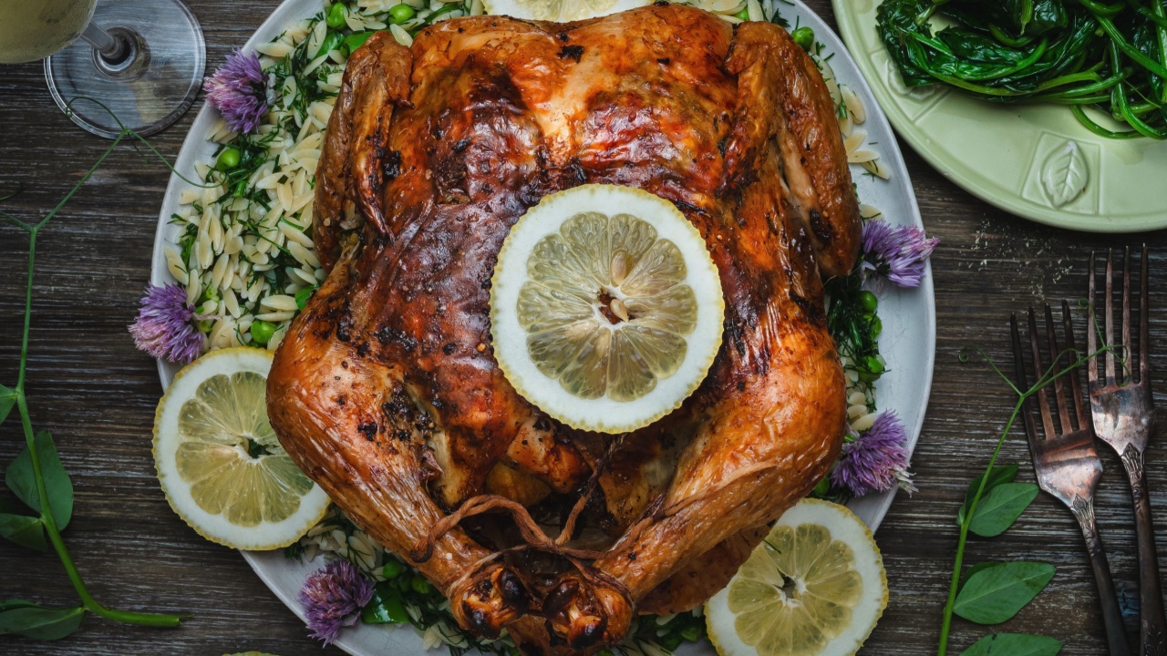 Whole roasted chicken on a plate with orzo, lemons, herbs and sauteed spinach.