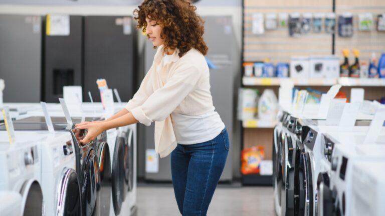 Customer selecting new washing machine in appliance store, examining features and making purchasing decision