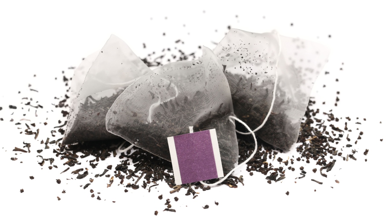 Transparent pyramid mesh black tea bag with violet tag, isolated on white background