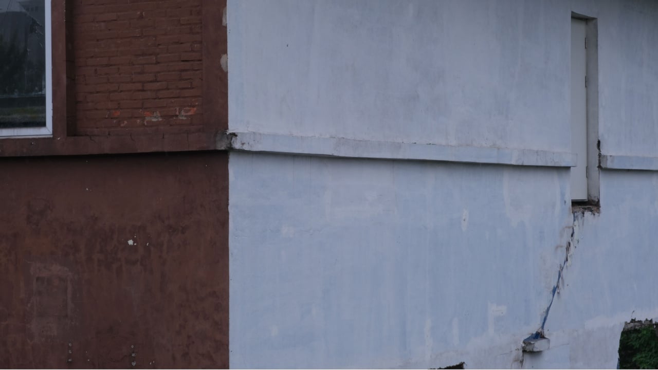 "Exterior wall of a building with a large visible crack, showing structural damage."