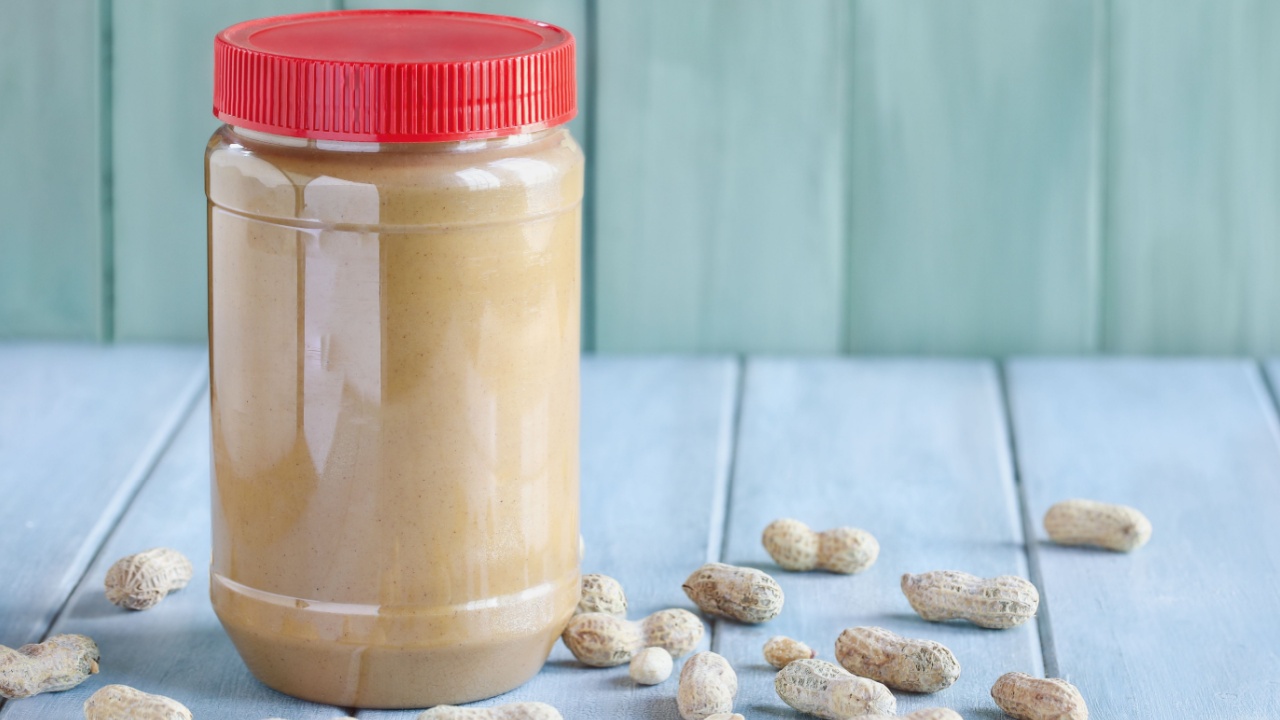 Front view of a full jar of peanut butter over a blue table with copy space and green background. Selective focus with blurred background.