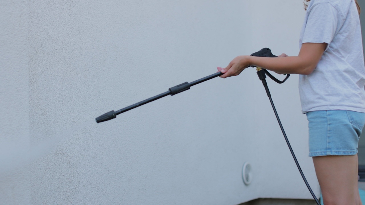 Young woman wash house wall with pressure washer.