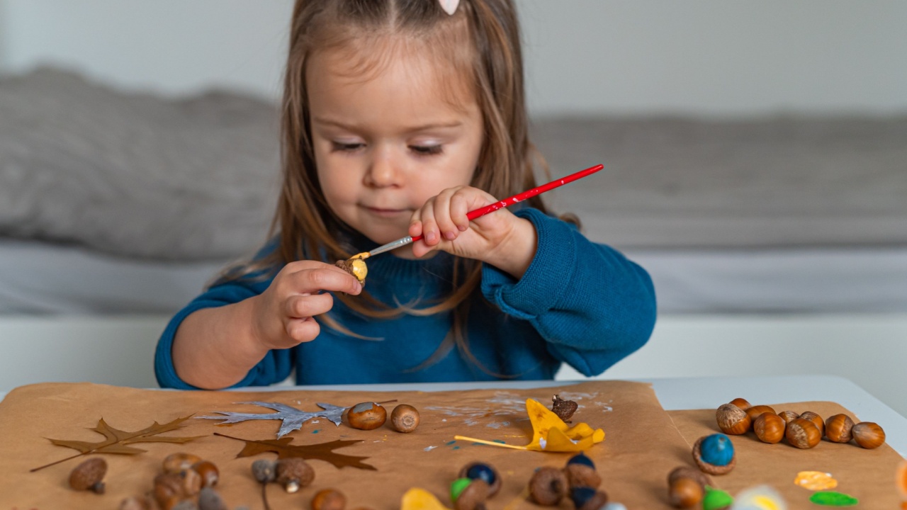Cute toddler girl painting acorns with a brush for a craft project