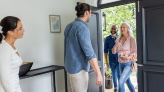Welcoming guests at home, smiling couple greeting friends at front door. Hospitality, friendship, reunion, arrival, interaction, gathering