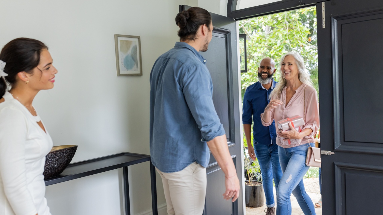 Welcoming guests at home, smiling couple greeting friends at front door. Hospitality, friendship, reunion, arrival, interaction, gathering