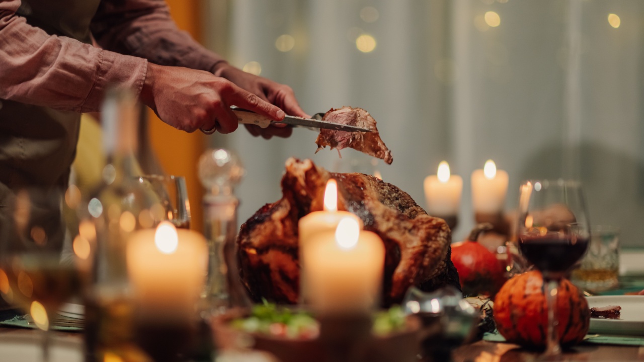 Chef carves a roasted turkey at a thanksgiving dinner table illuminated by warm candlelight, surrounded by festive decorations