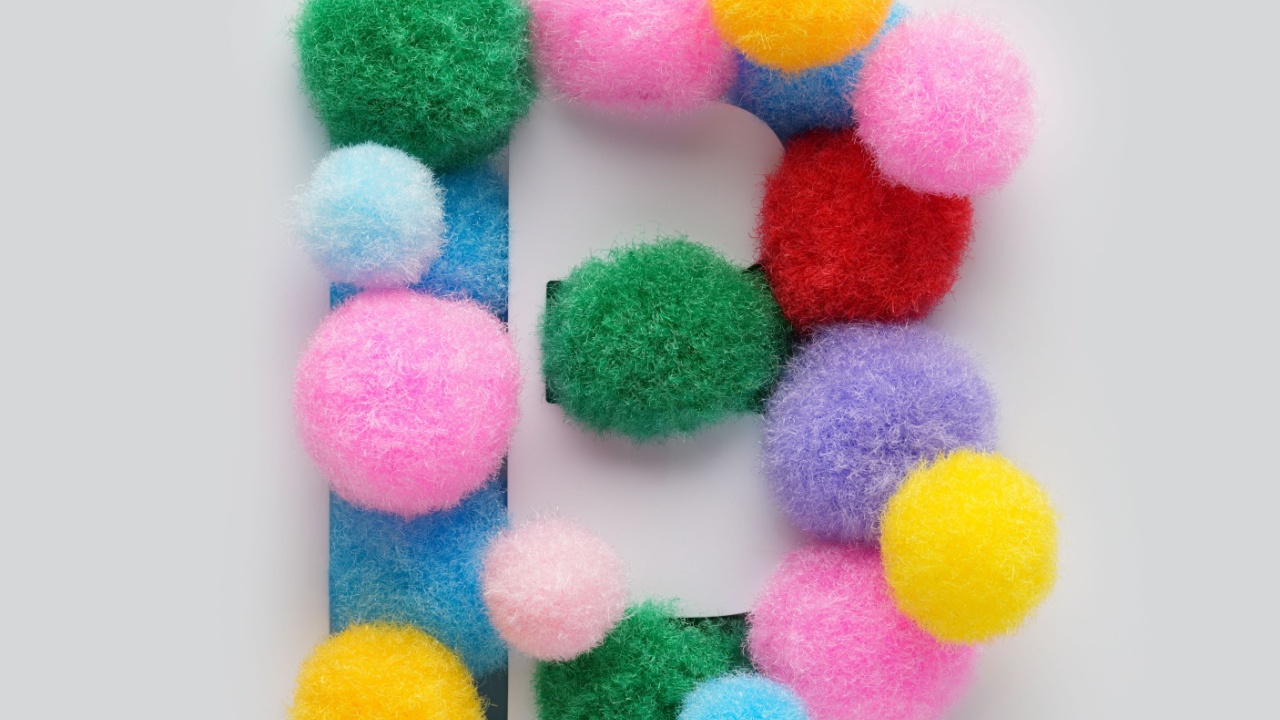 Colorful letter B made of fluffy pom poms on white background. Creative handmade typography for kids learning alphabet, educational design, playful classroom decor, and graphic projects.