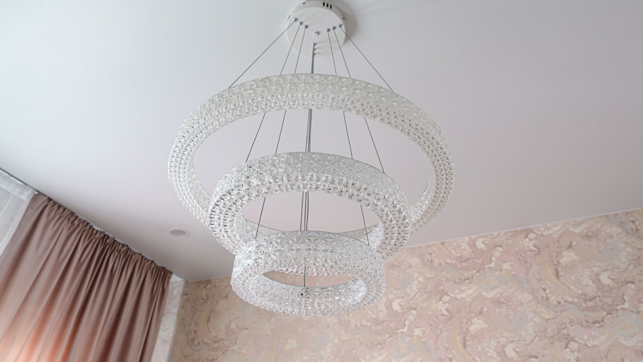 Low angle shot of a modern three-tier crystal ring chandelier against a white ceiling and pink-swirled wallpaper