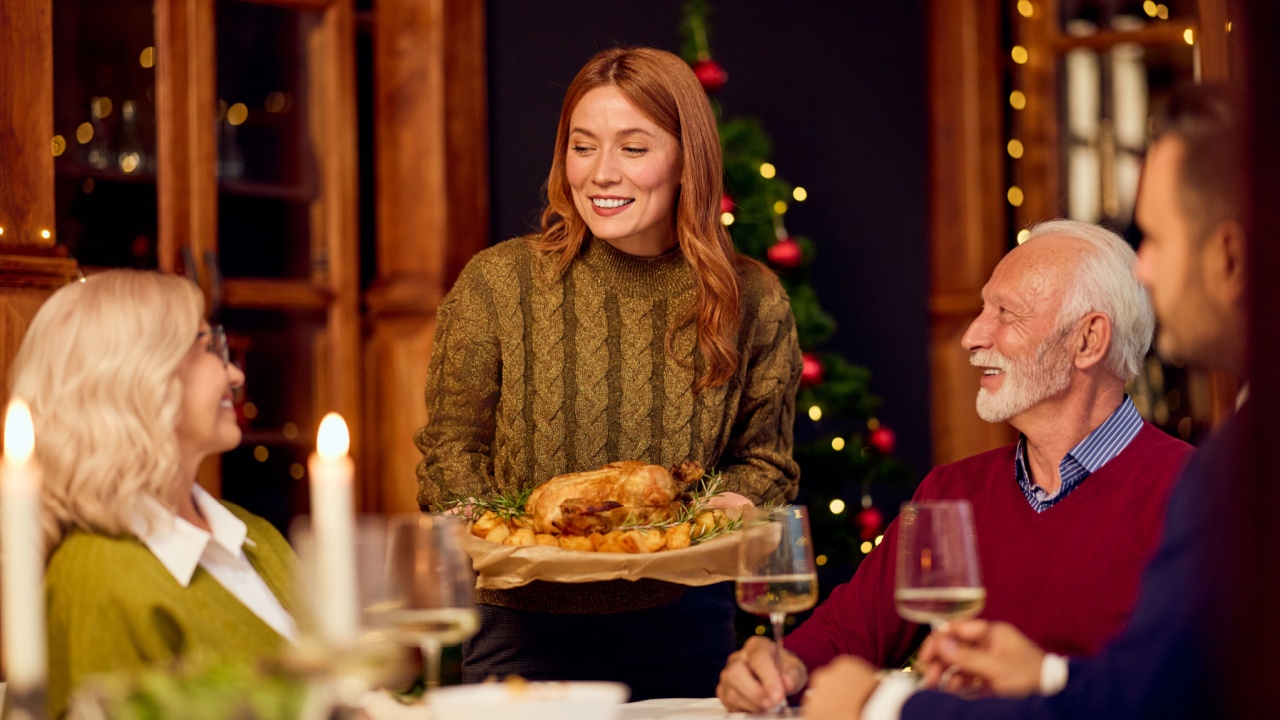 Cozy holiday dinner as a server brings a roasted feast to a joyful family gathering near a Christmas tree.